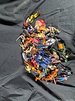 Top view of assorted vintage plastic toys and figures scattered on a black backdrop showing variety of figures including animals, superheroes, and fantasy characters.