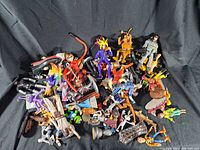 Top view of mixed vintage and used plastic action figures in various colors, including characters with cloaks, swords, and fantasy costumes spread on black background.