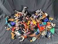 Top-down photo of assorted action figures and toys spread out over a black cloth, showing various characters from superhero and sci-fi genres.