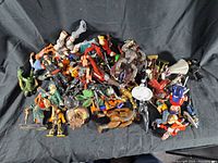 A large pile of assorted vintage and used action figures and toys of varying character types and styles on a black cloth background.