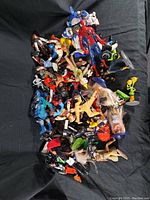 Top-down view of assorted action figures in bin, showing variety including Spider-Man and other superhero toys