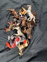 Top-down view of vintage toy horses and knight figures piled in a black fabric background showing variety of colors and details