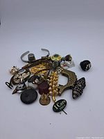 Photo of assorted vintage costume jewelry pieces including cuff bracelets, clip-on earrings, decorative pins, and rings in various designs and materials.