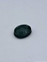 Single oval faceted emerald gemstone on white background showing surface wear and deep green color.