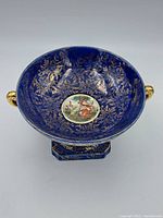 Angled view showing the blue and gold floral interior with central painted scene and two gold handles