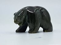 Side view of a small dark green jade bear figure showing smooth polished surface and carved detail on face and legs.
