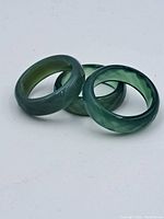 Three jade rings arranged on a white surface showing different shades of green and polished band shapes.