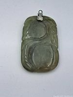 Front view of rectangular jadeite pendant with organic carved abstract design attached to sterling silver clasp.