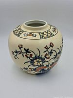 Round, bulbous cream-colored Japanese porcelain vase showing hand-painted floral motifs in colors like red, blue, green. The neck area has geometric lattice patterns. Vase surface appears aged but intact.