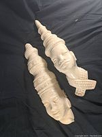 Two large carved Asian stone head sculptures lying side by side on black fabric background, showing textures and fine details of the headdresses and faces.