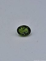 Close-up image of a single oval cut green peridot gemstone showing natural inclusions and facets.
