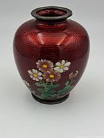 Front view showing the red cloisonné vase with hammered texture and floral painting.