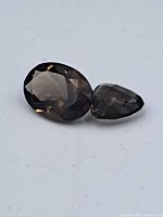 Two loose faceted smokey quartz gemstones on a white background. Gemstones show medium-dark brown color and faceting details.