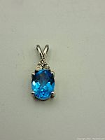 Front view photo of sterling silver pendant with oval blue stone showing prong setting and decorative top.