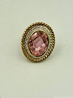 Front view of vintage sterling silver ring with oval faceted pink stone surrounded by small clear stones and gold-tone rope border.