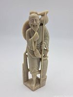 Front angle of the carved stone figure showing the man with staff and smiling face.