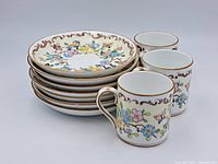 Three decorated fine china cups stacked with seven matching saucers underneath, showing floral and butterfly designs with gold accents.