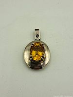 Topaz sterling silver pendant front view showing the faceted yellow-orange oval gemstone with a polished silver frame and engraved bale.