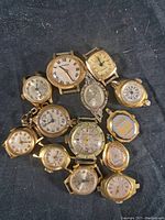 Front view of 13 variously shaped gold-tone vintage watch faces with Roman numerals and numbers visible in used condition.
