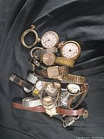 Lot items arranged on dark cloth include multiple wristwatches and pocket watches, various watch types and bands visible.
