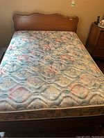 Full view of the bed showing the wooden headboard, mattress, and boxspring with floral pattern