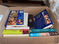 View of a box with multiple cookbooks and novels, showing titles and book spines.
