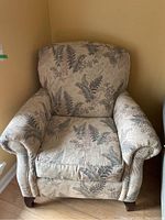 Front view of the upholstered armchair showing the floral leaf pattern and rolled arms.