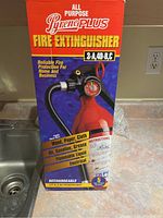 Boxed Pyrene Plus fire extinguisher showing front with red extinguisher and yellow and red text detailing fire types it fights.