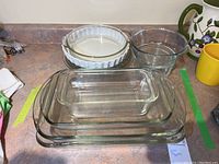 Clear glass baking dishes stacked including loaf pan, and mixing bowls with pie plates in background