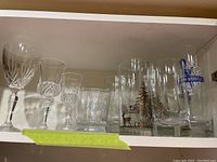 Shelf with assorted clear glassware including cut crystal, etched design glasses, and branded beer steins
