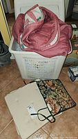 Plastic laundry hamper with bed covers inside and two cushions placed outside