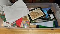 Plastic bin containing assorted folded placemats and tablecloths including a white piece and some Christmas themed linens.