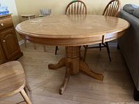 Wood pedestal dining table showing the base and part of the surrounding chairs.