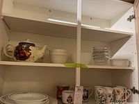 Shelved kitchenware showing teapot, bowls, Pyrex measuring cups, and mugs