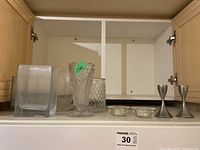 Glass vases, votive candle holders, and metal candle holders, displayed on a shelf inside a cabinet.