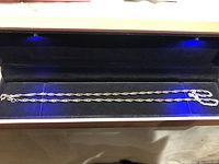 Silver necklace chain displayed in a black jewelry box under blue lighting for clear visibility of chain details.