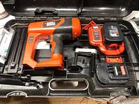 Black & Decker cordless staple gun nestled inside the plastic carrying case along with two batteries and a clamp attachment.