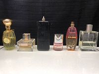 All six perfume bottles lined up on a flat surface showing variety of sizes, colors, and styles