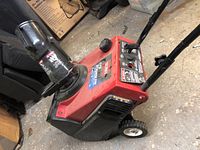 Photo showing the right side angle of the red Toro snow thrower with wheels, chute, and fuel cap visible.
