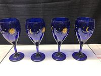 Four cobalt blue vintage wine glasses with celestial yellow sun, moon, and star designs lined up.