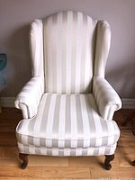 Front view showing wingback design, striped fabric upholstery, and wooden legs.