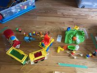 Overview of all items shown including train engine, train cars, animal and human figures, circus wagon, and green playset parts on wooden floor.