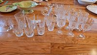 Photo showing assorted clear crystal and glassware including tall and short glasses, wine and champagne glasses with stems, and a brandy snifter glass.