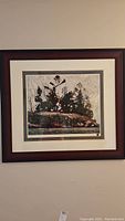 Front view showing the framed print featuring evergreen trees and rocky shoreline in earthy tones.