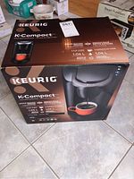 Full front view of Keurig K-Compact coffee maker box showing product image and features.