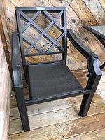 Full view of one black metal patio chair with lattice backrest and armrests on wooden deck.