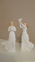 Photo of two white porcelain Royal Doulton figurines, one holding a dove and the other releasing one.