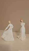 Two Royal Doulton porcelain figurines displayed on a plain surface, showing their full form and white dresses.