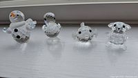 Photo of four Swarovski crystal figurines lined up including a snowman with orange nose, a duck with black eyes, a pufferfish with black eyes and fins, and a koala with black eyes and rounded ears.