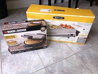 Photo showing boxed Black & Decker Belgian Waffle Maker and Bella Triple Buffet Server boxes on tile floor.